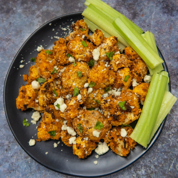 Overhead shot of buffalo cauliflower on a black plate garnished with herbs and celery on the side. 