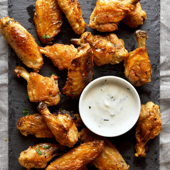 Air fryer chicken wings arranged on a linen tablecloth around a bowl of ranch dip in a white bowl.