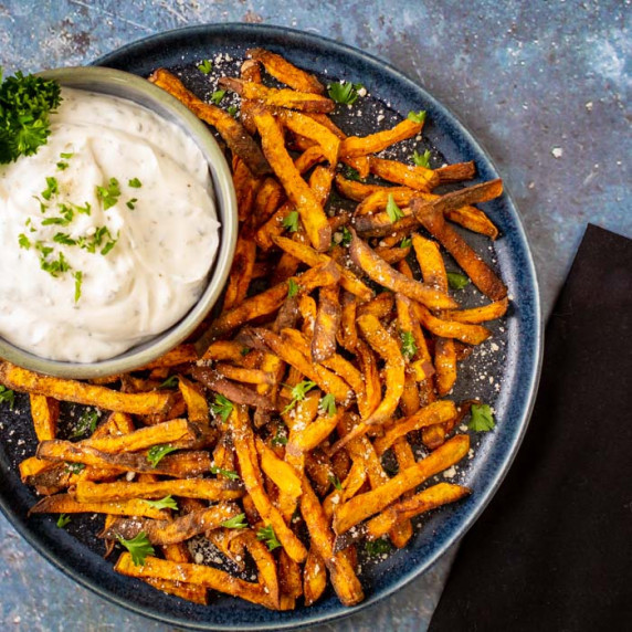 Top down view of sweet potato fries piled on a blue plate with a side of ranch mayo and a black napk