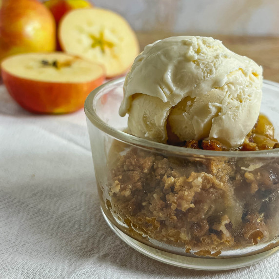Apple Crisp in a glass bowl topped with vanilla ice cream with apple halves behind.