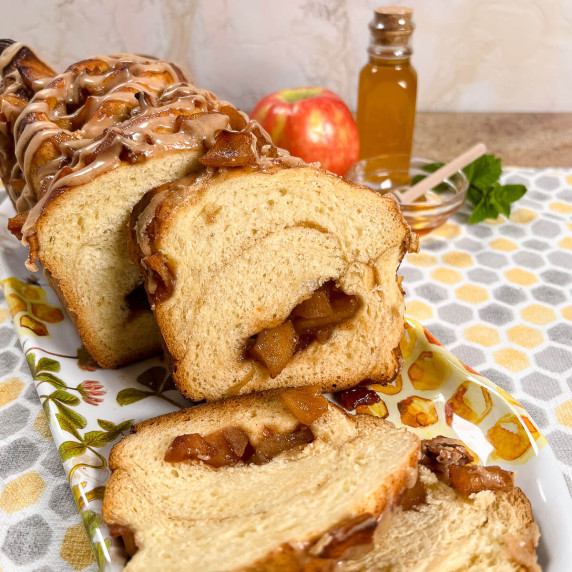 Sliced apple honey babka on a plate with an apple and honey in a jar and bowl behind.