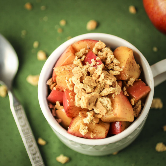 Overhead shot of apple pie snack in a white mug with a spoon and graham cracker crumbles on the side