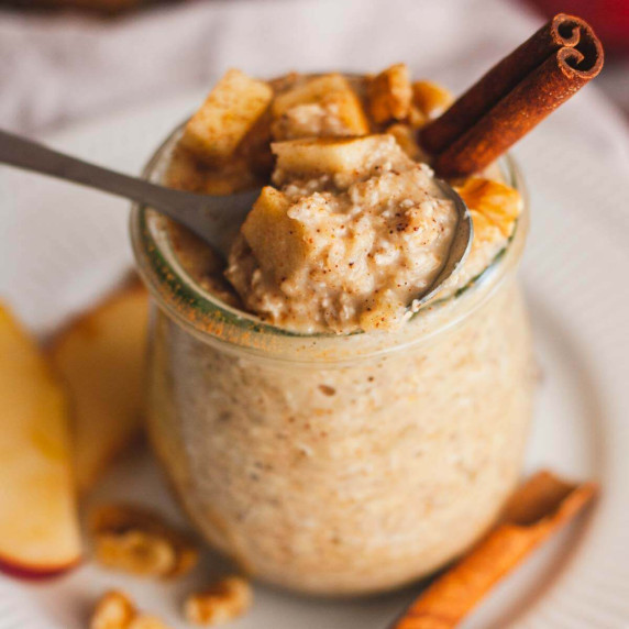 A closeup of a jar of applesauce overnight oats topped with chopped apples and a cinnamon stick.