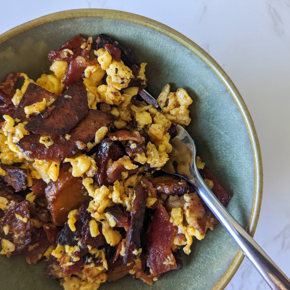 A bowl of scrambled eggs, potatoes, and bacon