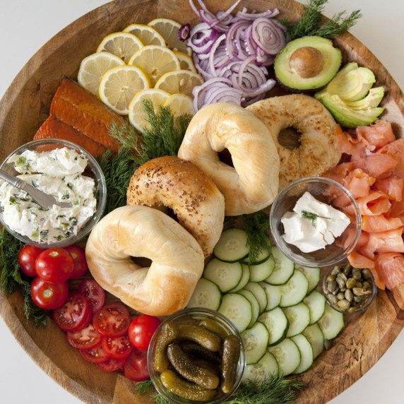 Bagels, cream cheese, salmon, tomato, avocado, dill, and more on a beautiful board