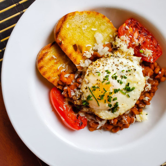 Golden toast, bright red tomatoes, baked beans, and an egg with green herbs.