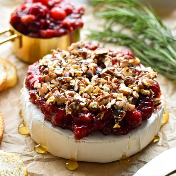 baked brie topped with cranberry sauce, nuts and honey on parchment paper.