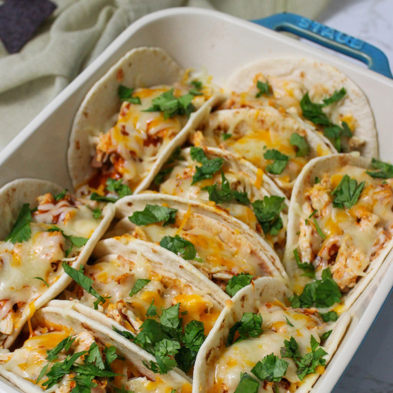 A baking dish full of cheesy baked soft shell chicken tacos garnished with cilantro