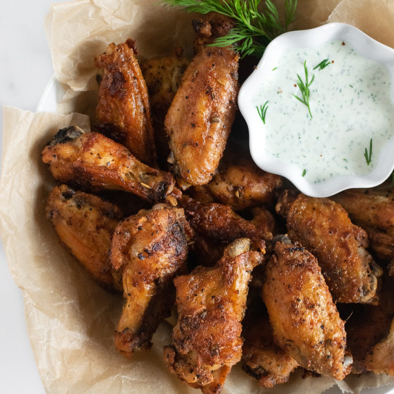 baked chicken wings in a basket with a cup of homemade ranch dressing