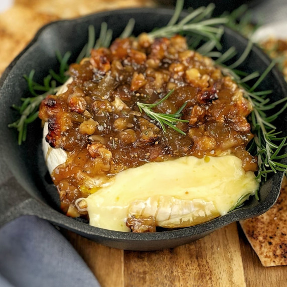 Wheel of brie cheese in a small cast iron skillet on a wooden board showing the cheese melting on on