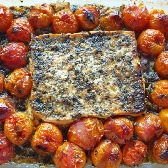 baked feta at the center of a baking tray with roasted cherry tomatoes.