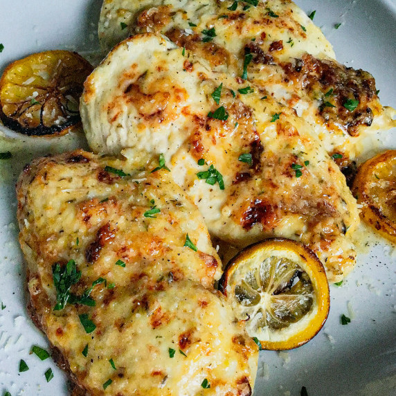 Baked chicken breasts with parmesan and lemon topping and sliced roasted lemons. 