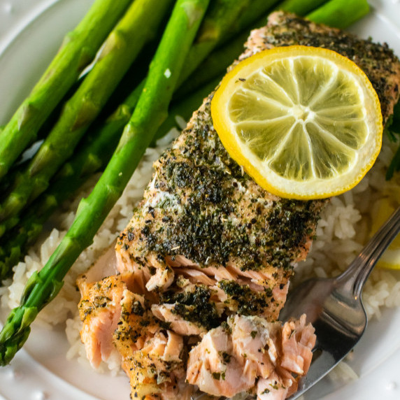 baked salmon with a fork on a white plate with rice and asparagus.