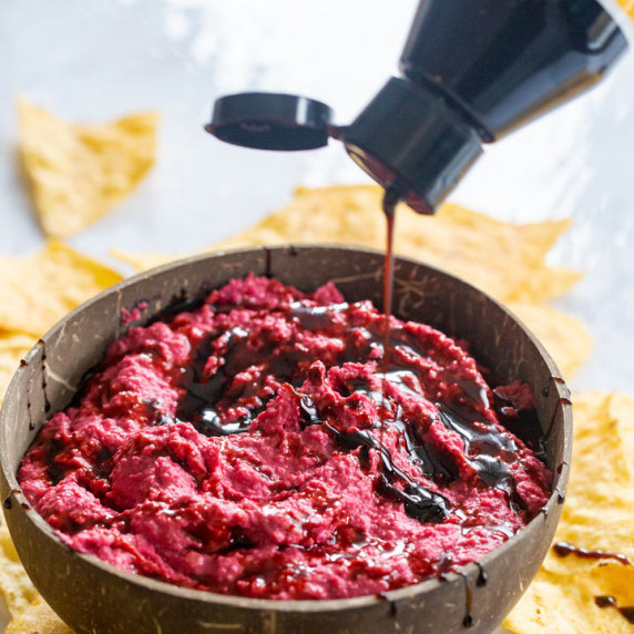 beet hummus being drizzled with a store bought balsamic glaze in a coconut bowl