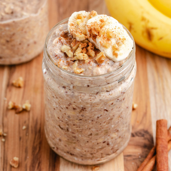 Cinnamon and banana overnight oats in a glass jar with sliced banana on top.