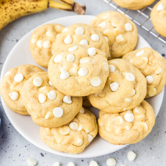 Square view of a plate of banana pudding cookies topped with white chocolate chips on a counter.