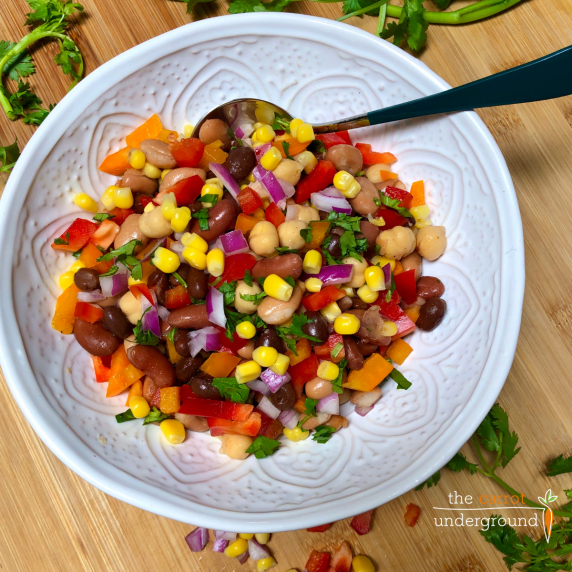 A bowl filled with bean salad made with beans, red and orange peppers, corn, red onion, & cilantro.