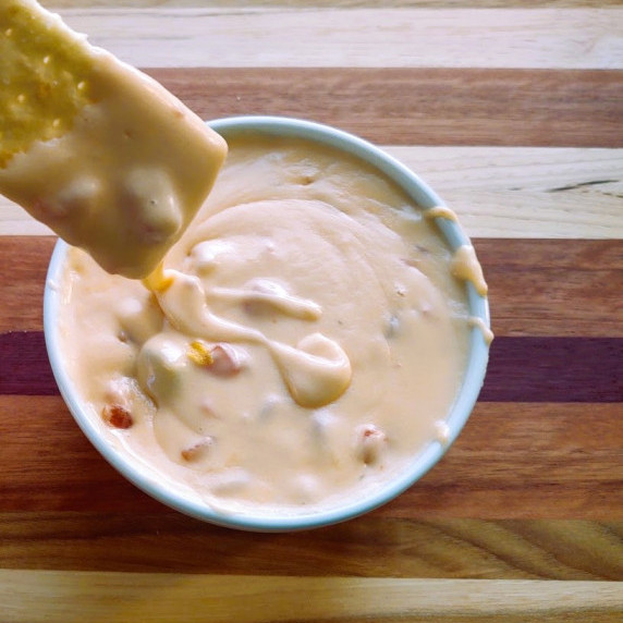 Beer cheese dip dripping off of a cracker that was just dipped into the cheese.  
