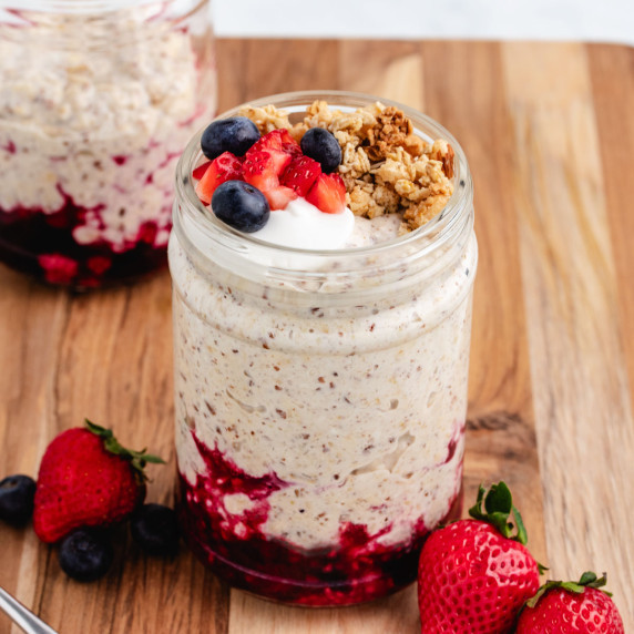 A jar with mixed berry cheesecake overnight oats with granola and berries on top.