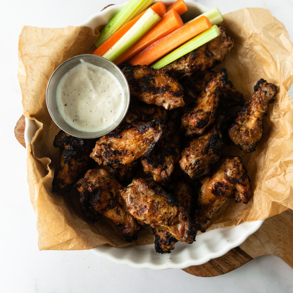 grilled chicken wings on a white platter with celery, carrots and blue cheese dressing.