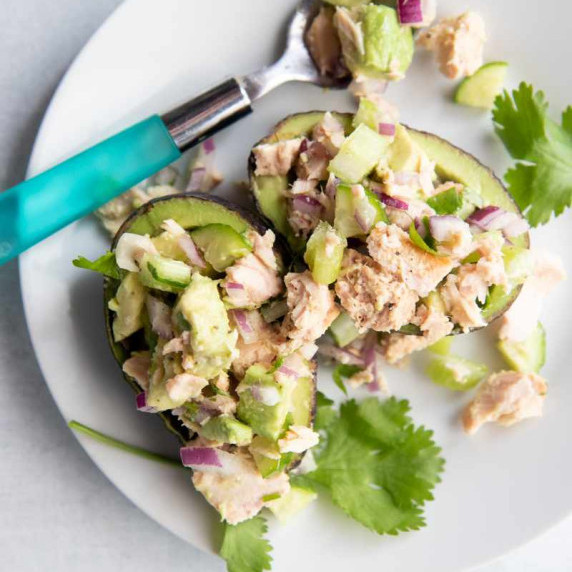 Tuna salad made with avocado and red onion stuffed into avocado halves on a round, white plate.