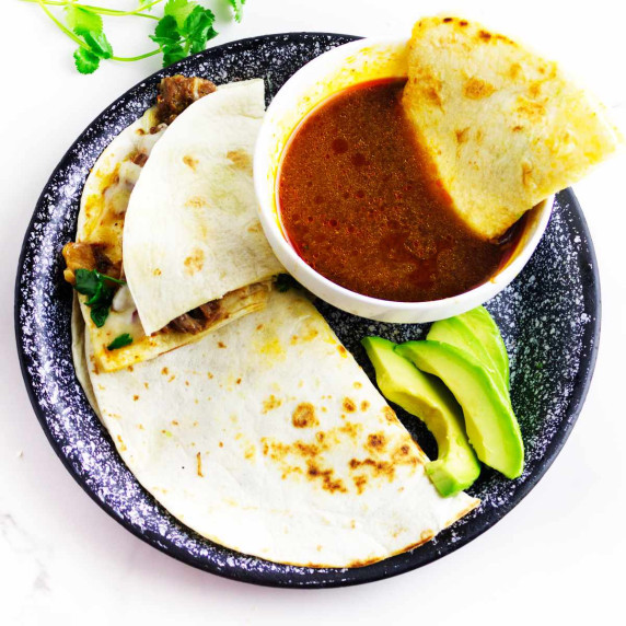 platter of beef birria quesadilla and consume with sliced avocados.