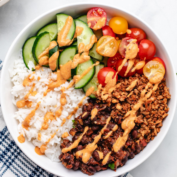 Black bean burrito bowl with rice, vegan ground meat, cucumbers, tomatoes, and vegan chipotle sauce.