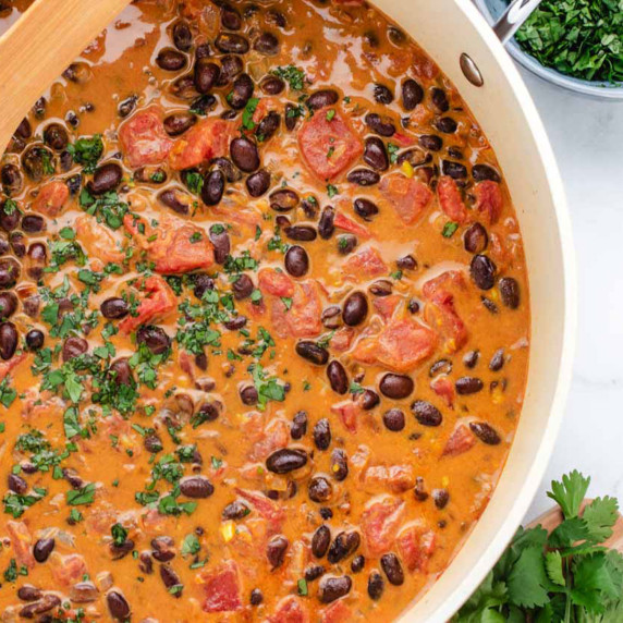 Black bean curry in a pan with a wooden spoon and chopped cilantro.