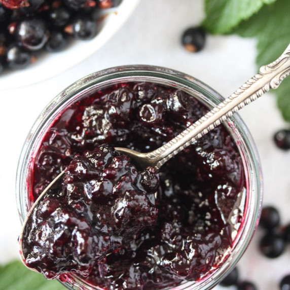 Shiny black currant jam in a small jar with a vintage spoon on top.