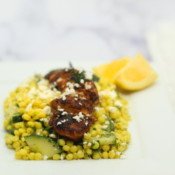Sliced blackened chicken on a bed of cucumber couscous salad on a white plate.