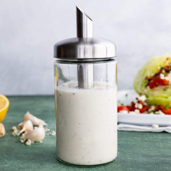 A glass cruet of homemade blue cheese dressing stands on a counter in front of a plated wedge salad.