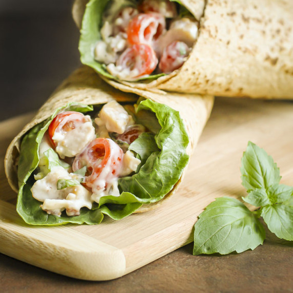 Side close up shot of blue cheese chicken wraps on a wooden cutting board with basil on the side.