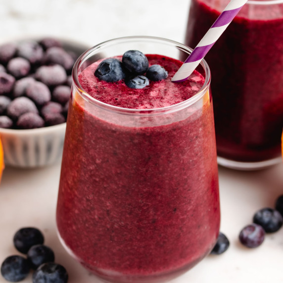 A blueberry beet smoothie in a glass with a straw and blueberries on top.