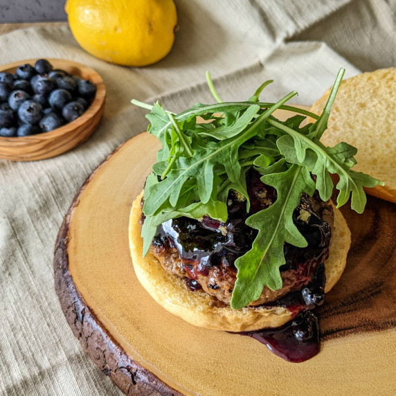 A burger on a serving stump topped with blueberry jam and fresh arugula