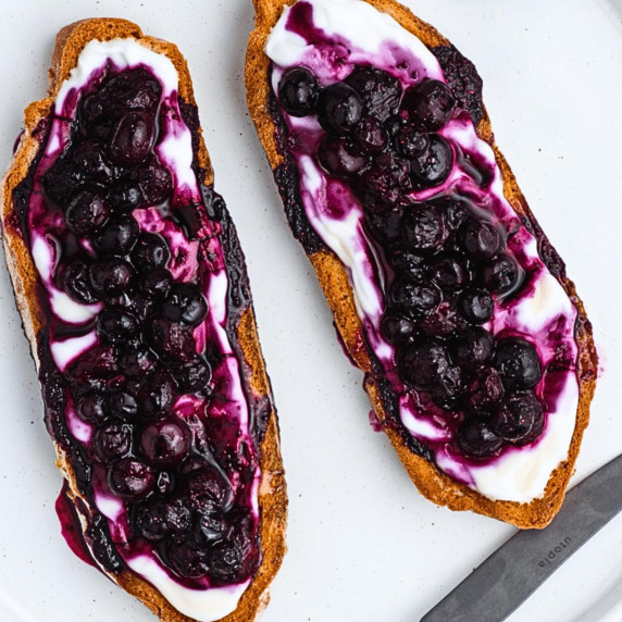 blueberry sauce on toast with greek yogurt, a butter knife on the side on a white countertop