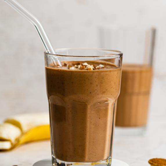 Banana Almond Butter Smoothie With Cinammon in an aesthetic glass with straw and banana on the side