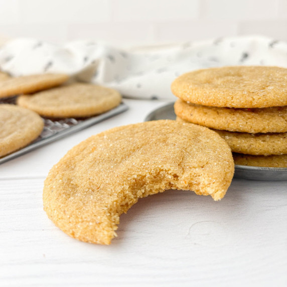 Closeup of Brown Butter Sugar Cookie with a bite missing with stacked cookies in the background.