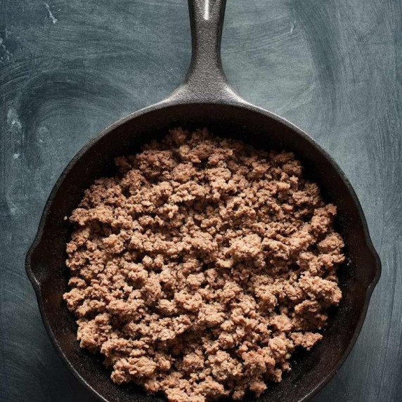 Birdseye view of cooked ground beef in a cast iron skillet on a dark countertop.