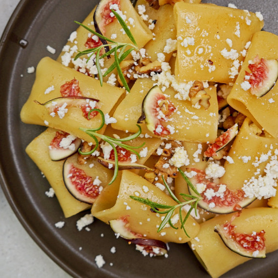 A bowl of brown butter pasta topped with golden butter sauce, crunchy nuts, figs, and crumbled feta.