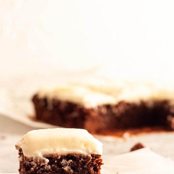 A close up of a slice of chocolate brownie with cream cheese frosting.