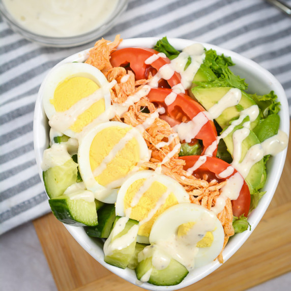 Side close up of buffalo chicken salad with blue cheese dressing in a white bowl on a grey cloth.