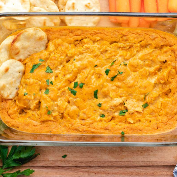 Buffalo chickpea dip in a glass dish with crackers and carrots.