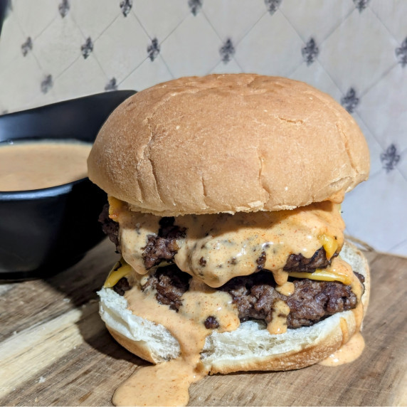 A double cheese burger with BBQ burger sauce dripping off it. 