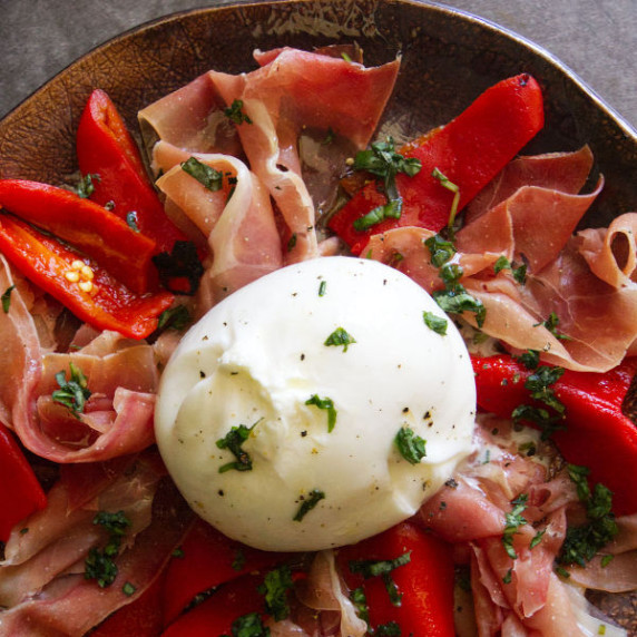 A Barrata cheese cball sits on a bed of Serrano Ham and Roasted red peppers