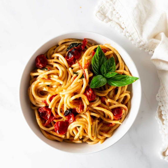 spaghetti with cooked cherry tomatoes and basil in a white bowl.