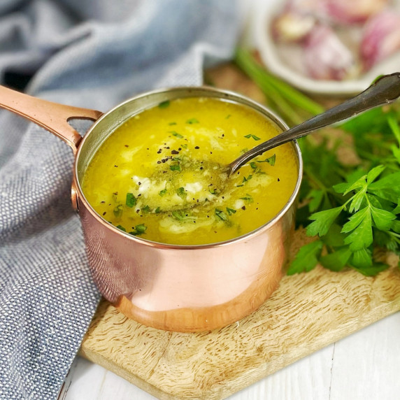 melted butter and garlic sauce with parsley in a small copper pot on a wooden board with a spoon