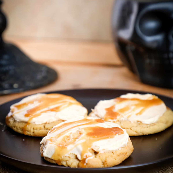 3 butterbeer cookies on a plate topped with buttercream and a caramel drizzle.