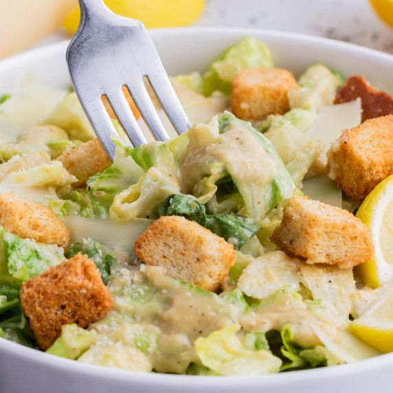 Caesar Salad Dressing RECIPE served with salad in a white bowl with a fork.