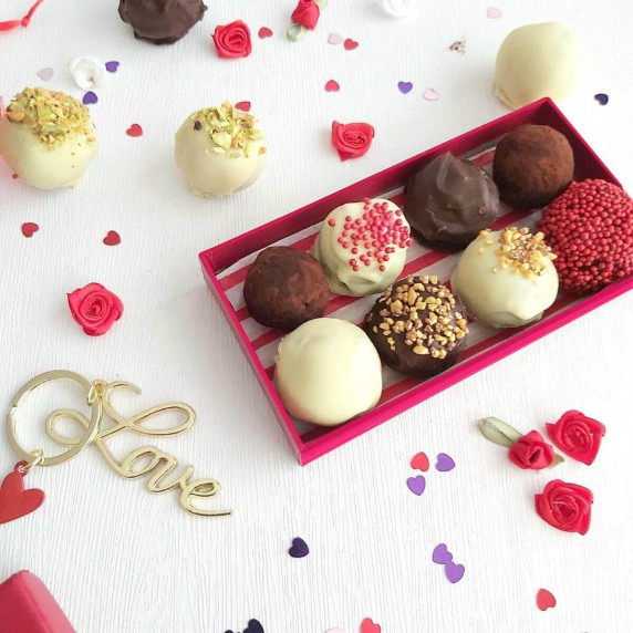 Image of a white table with Valentine heart sprinkles surrounding a red box of homemade cake truffle