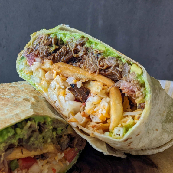 Two halves of a burrito stuffed with steak, avocado, french fries, and cheese